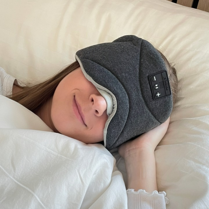 Ung kvinne som hviler i sengen med Dreamli Bluetooth sovemaske som skjermer lys og gir roligere søvn.